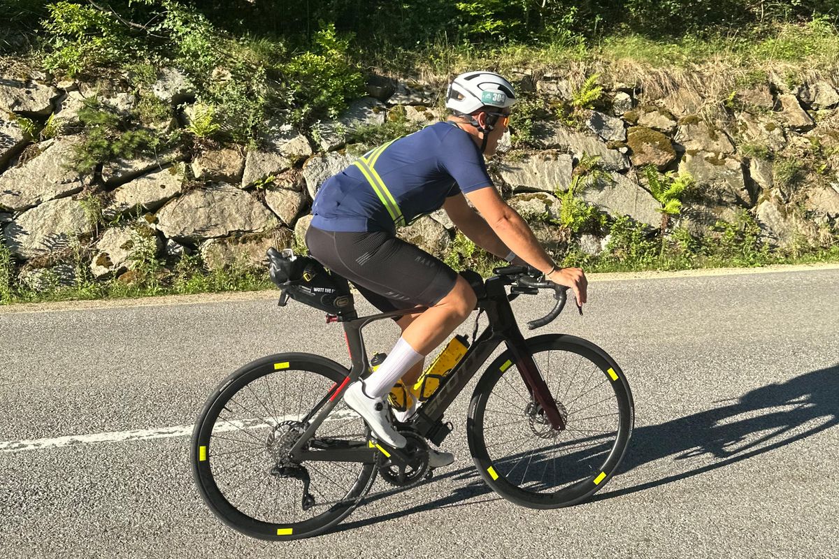 Martin auf dem Rennrad vor einer bewachsenen Steinmauer, gelbe Warnweste über dem Trikot, Startnummer 304 am Helm, Satteltasche und kein Auflieger am Lenker