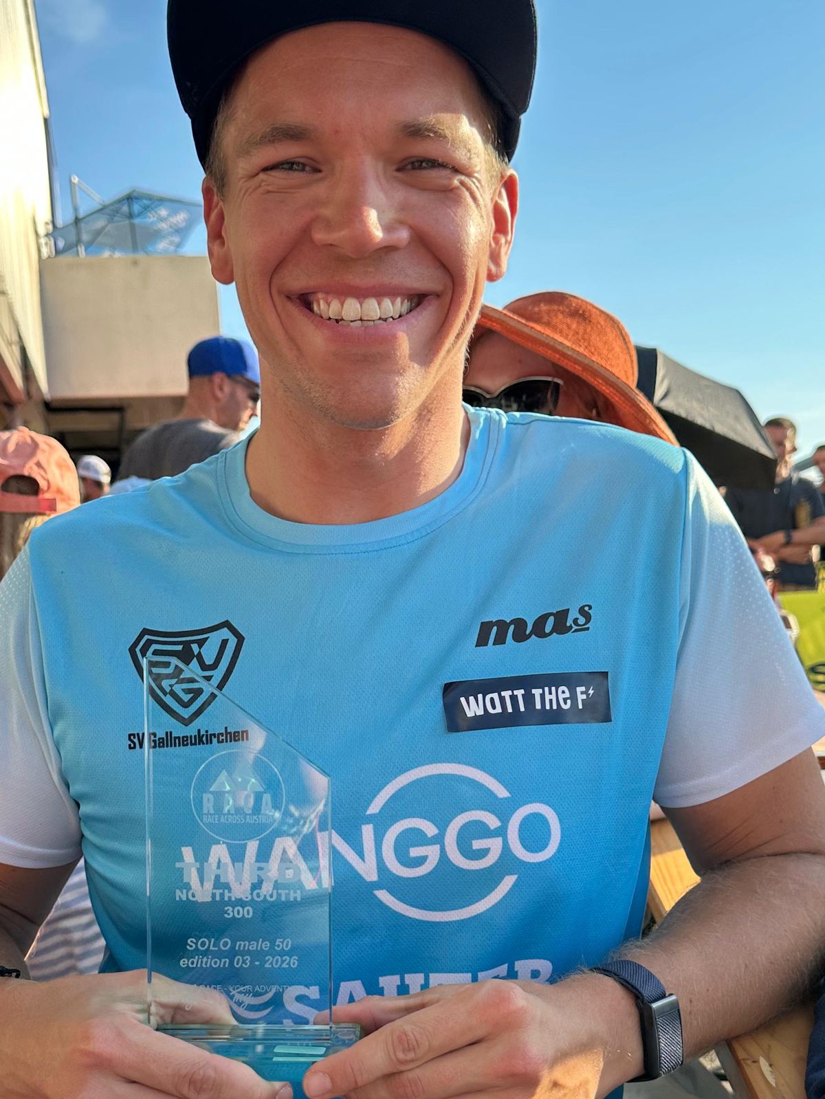 Martin mit schwarzer Kappe und hellblauem Shirt lacht in die Kamera und hält einen Glaspokal mit der Aufschrift Third, North-South 300