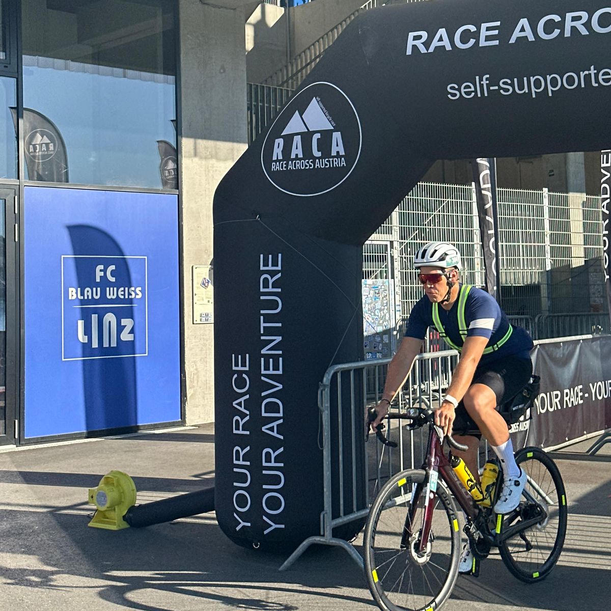 Martin rollt mit Warnweste aus dem aufblasbaren Startbogen des Race Across Austria, links das Schild des FC Blau-Weiß Linz