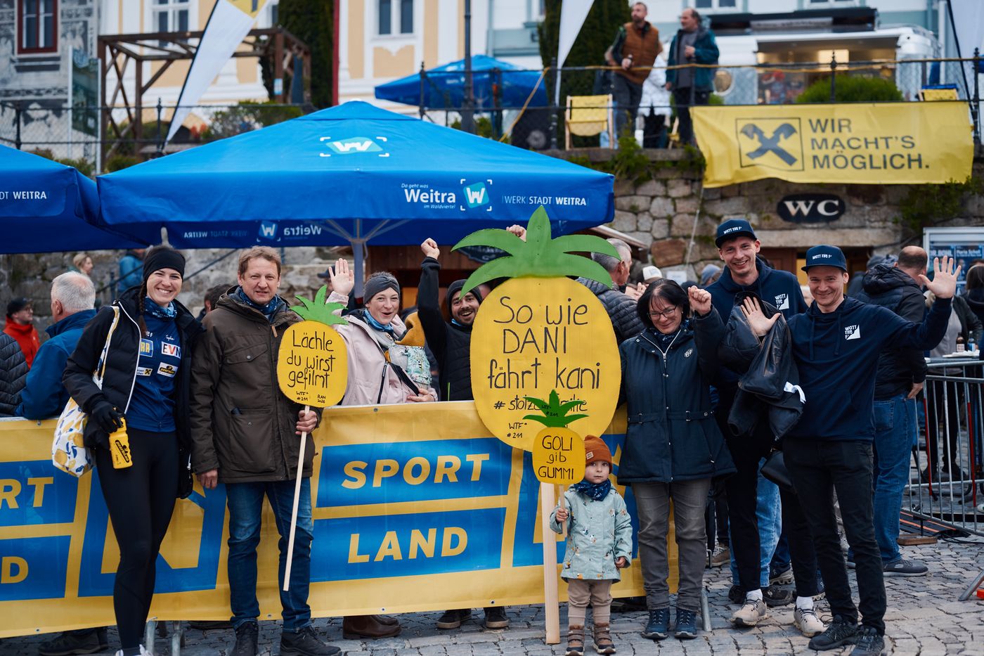 Fans hinter einer Sportland-Banderole mit selbstgemalten Schildern, eines davon mit der Aufschrift So wie Dani fahrt kani