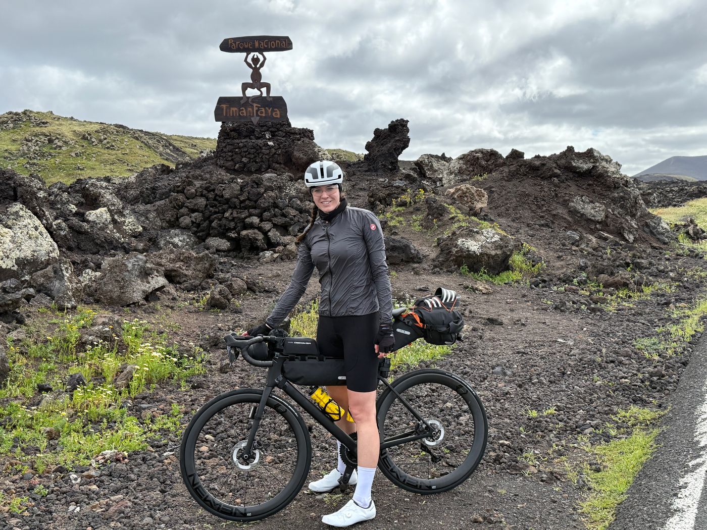Dani mit ihrem bepackten Rennrad vor Lavafelsen und dem Schild des Timanfaya-Nationalparks