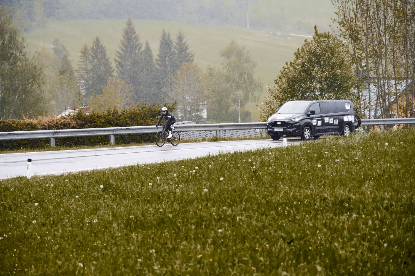 Ein Fahrer allein auf nasser Landstraße im Regen, dahinter das schwarze Pacecar